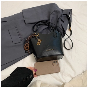 Detalle de bolso tipo cubo negro con colgante de ábaco dorado y accesorio de correa tejida