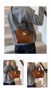 Détail d'un sac seau en cuir marron avec boucle dorée et foulard en soie sur la poignée