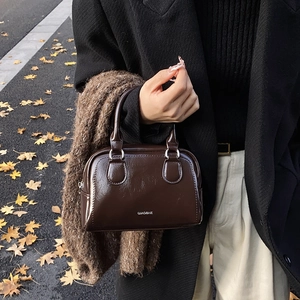 Minimalist dark brown glossy leather bowling bag held by a model on an autumn street