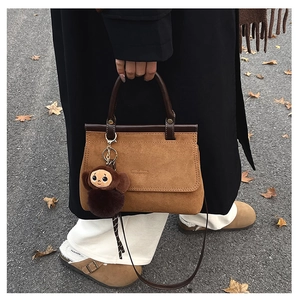 Détail d'un sac à main en daim marron avec breloque singe en peluche sur rue d'automne