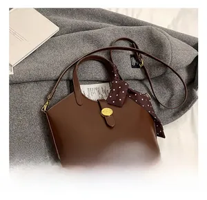 Détail d'un sac à main marron foncé avec fermoir doré et foulard à pois sur la poignée
