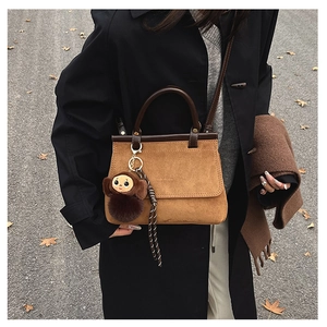 Détail d'un sac cabas en daim marron avec pendentif en peluche dans un décor d'automne