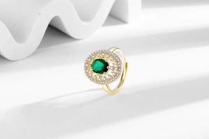 Macro detail of luxury gold ring featuring oval emerald gemstone and zircon halo