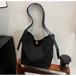 Minimalist black suede bucket bag with gold hardware on a wooden shelf in a lifestyle setting