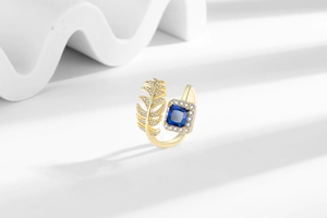 Detail of 18K gold ring with leaf design and square-cut blue gemstone on white base