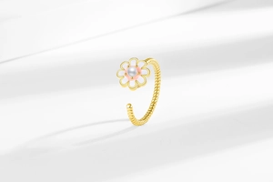 Dettaglio dell'anello a margherita dorato con petali bianchi, cuore rosa e perla centrale