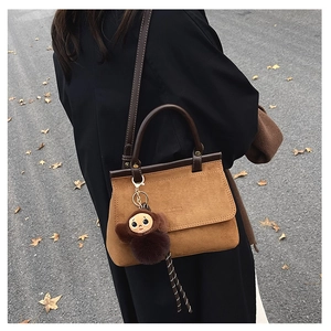Détail d'un sac bandoulière en daim marron avec poignées en cuir et breloque singe