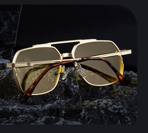 Close-up of golden aviator sunglasses with yellow lenses on a black stone base