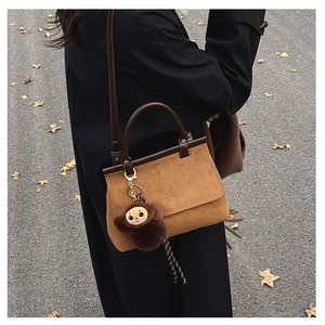 Détail du sac bandoulière en daim camel avec bordure en cuir marron et breloque singe