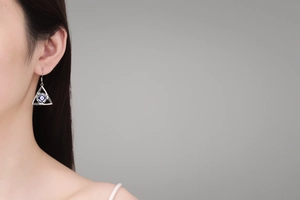 Detail of silver triangle evil eye drop earrings worn by a model in a boho style