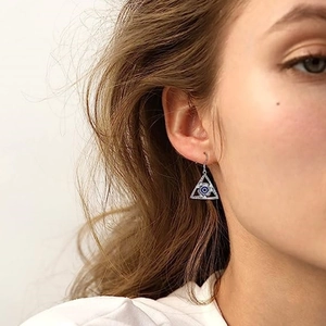 Close-up of a silver triangle evil eye drop earring worn by a model in a gothic style