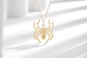 Close-up of gold spider pendant necklace with hollow legs on minimalist white display