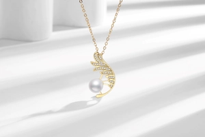 Detailed macro shot of a gold feather pendant with sparkling zircons and a white pearl