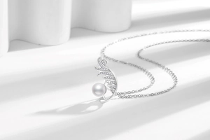 Detail of silver feather pendant necklace featuring micro-set zircons and a round white pearl