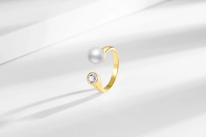 Close-up of golden open ring featuring a lustrous white pearl and sparkling zircon stone