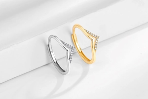 Detail of silver and gold V-shaped zircon rings on a white geometric background