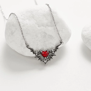 Macro shot of silver gothic bat necklace with red faceted heart pendant on white stones