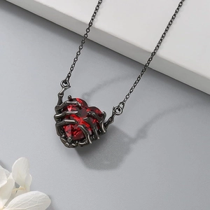 Gothic necklace featuring a red faceted heart stone held by black metal skeletal hands