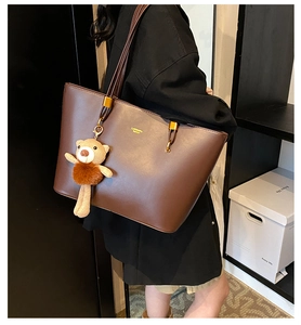 Detail of a large brown tote bag on shoulder with a cute knitted bear charm