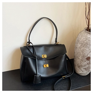 Detail of black matte leather handbag with gold twist lock and tassel charm on a wooden table
