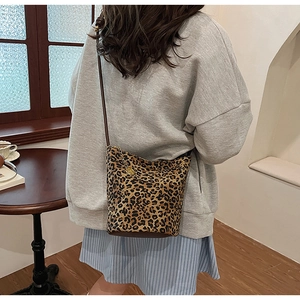 Detail view of leopard print bucket bag with brown leather bottom on a fashion model