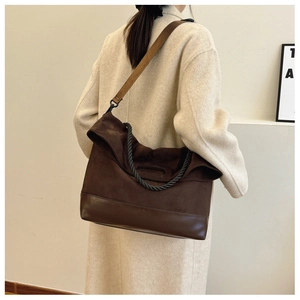 Detail of a large brown suede tote bag with braided handles and adjustable strap