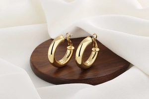 Detailed view of thick 18K gold plated hoop earrings on wooden display and silk