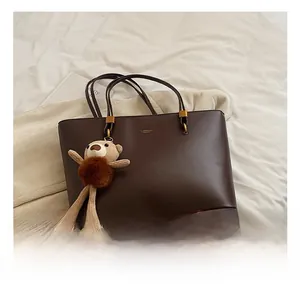 Detail showing deep brown leather tote with fine gold hardware and plush bear charm