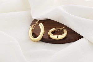 Detail view of chunky 18K gold plated hoop earrings with mirror finish on wooden stand
