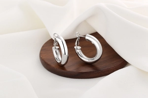 Macro shot of silver polished hoop earrings on a dark wood base with white silk