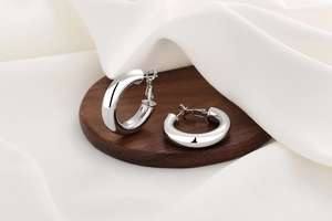 Polished silver hollow hoop earrings displayed on a dark wood base with silk background
