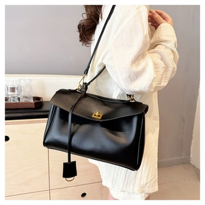 Close-up of black leather handbag featuring a gold twist lock and elegant leather pendant