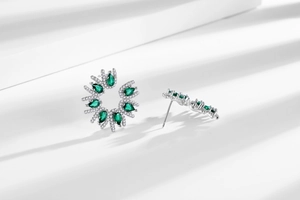 Close-up of snowflake flower stud earrings with green stones and sparkling diamonds