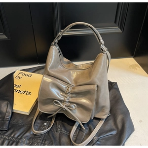 Detail of taupe glossy leather handbag with elegant bow and pleated texture on black leather