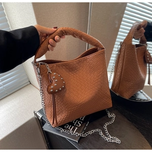 Détail du sac seau marron en cuir tressé avec chaîne argentée et breloque coeur