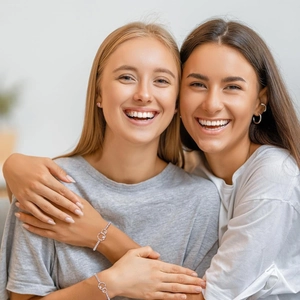 Silver bracelet with heart and interlocking rings pendant worn by two female models