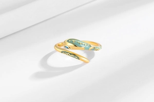 Macro detail of a gold snake ring featuring green enamel and a blue gemstone eye