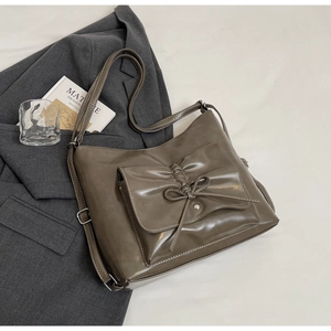 Detail view of khaki faux leather crossbody bag with bow tie decoration on a grey blazer
