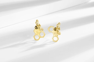 Macro detail of gold bee stud earrings with textured honeycomb base on white background
