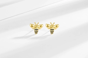 Macro shot of gold bee earrings with black enamel stripes on a soft grey surface