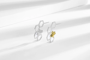 Detailed view of asymmetric honeycomb earrings with a small golden bee and silver finish