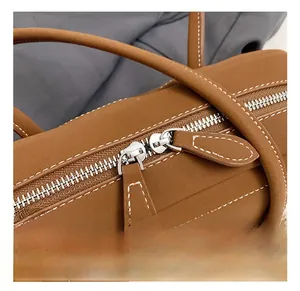 Detail of silver double zipper closure on brown suede tote bag with white stitching