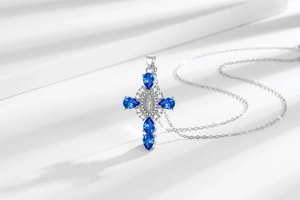 Detailed view of silver cross pendant with blue pear-cut gems and religious carving