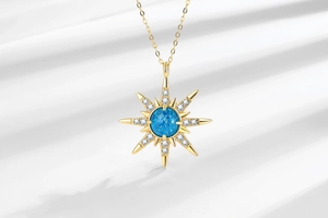 Detail of gold starburst pendant with blue gemstone and zircon on white silk fabric