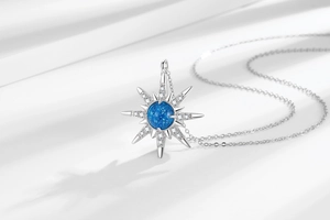 Macro detail of silver starburst pendant with a deep blue crystal on white silk fabric