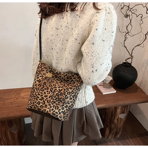 Detail view of large leopard print bucket bag with gold floral pendant on model