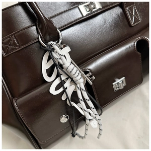 Detail of dark brown leather handbag with silver twist lock and woven charm accessories