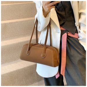 Detail showing the brown cylindrical leather tote bag with fine stitching and top zipper