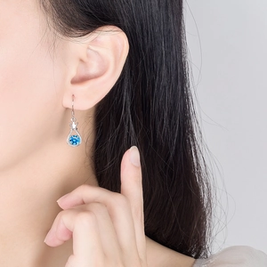 Silver drop earrings with blue zircon and crown detail worn by a model in a close-up view