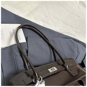 Detail of dark brown patent leather shoulder bag with silver hardware on blazer